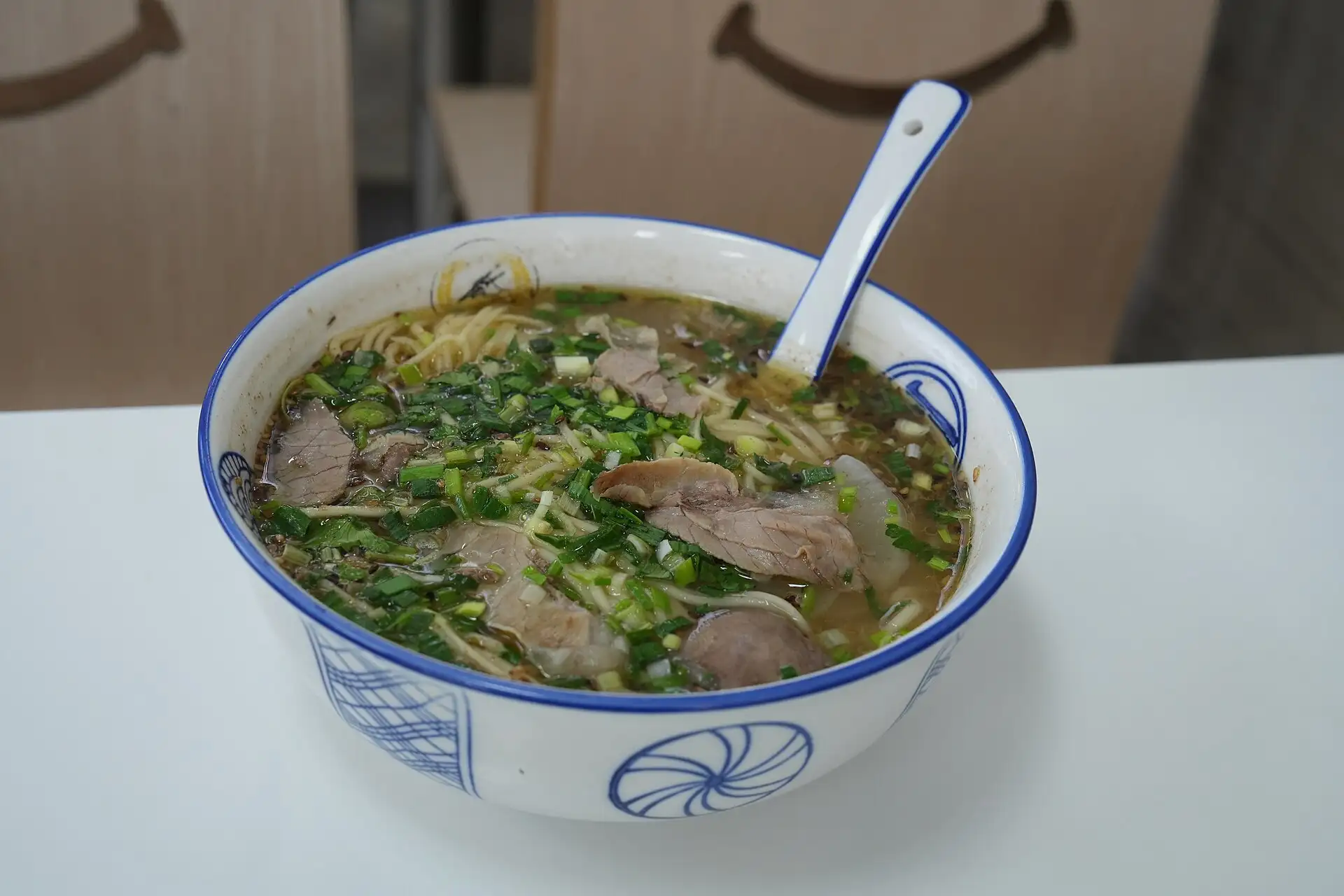 Schale mit Rindfleischnudelsuppe und Löffel auf einem weißen Tisch in Shenzhen